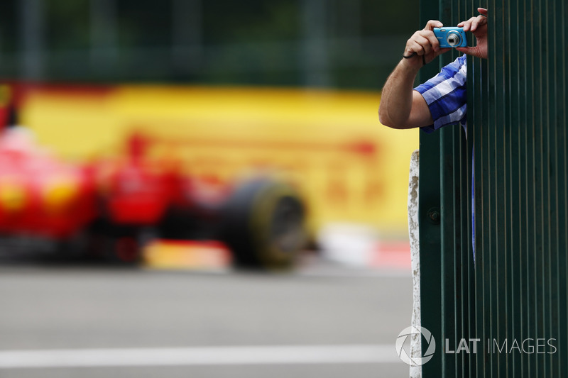 A fan leans out to take some photos as Kimi Raikkonen, Ferrari SF70H, passes through the background