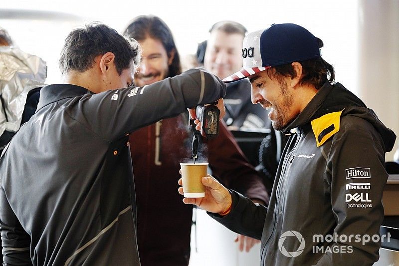 Lando Norris, McLaren, agita una taza de té con una herramienta eléctrica para Fernando Alonso, McLaren, mientras el conductor de IndyCar JR Hildebrand observa en el garaje