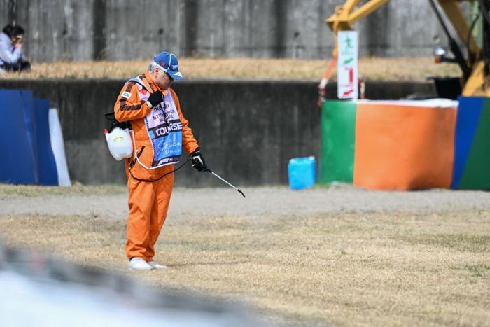 Un jefe de pista riega la hierba seca a lo largo de la pista