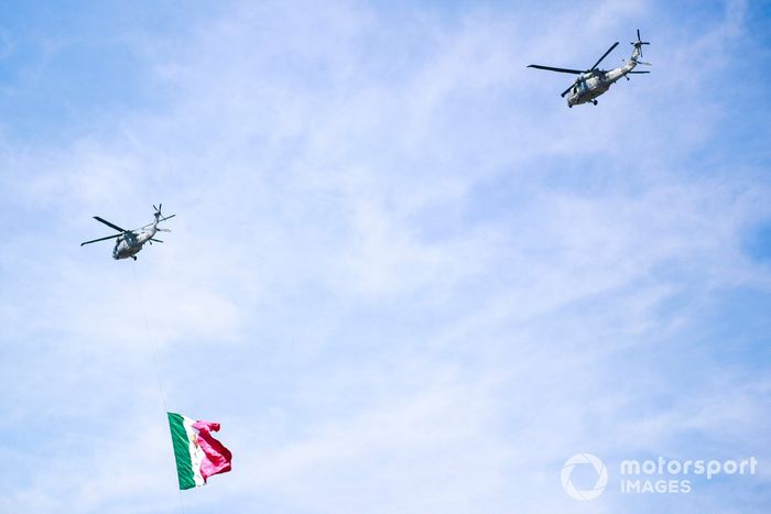 Un trío de helicópteros Sikorsky UH-60 Black Hawk de la Fuerza Aérea Mexicana sobrevuela la parrilla con una bandera mexicana antes de la salida