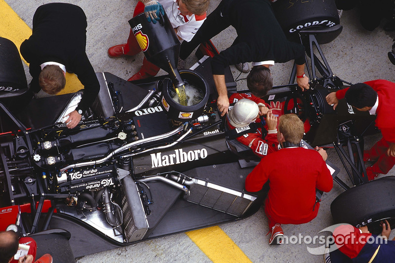 Alain Prost dans sa McLaren MP4/3 TAG Porsche pendant que les mécaniciens travaillent sur la voiture et la ravitaillent en essence